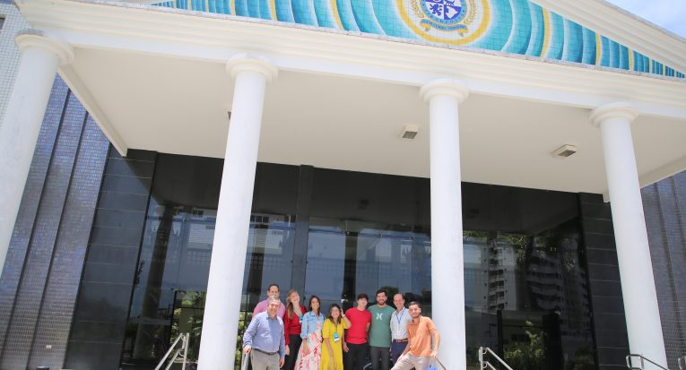 Grupo de aluno posam junto à comitiva da direção executiva em frente ao prédio da Reitoria da Unit