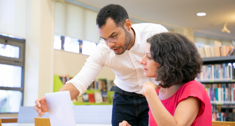 Instrutor a verificar o trabalho dos alunos na biblioteca _ Foto: Freepik